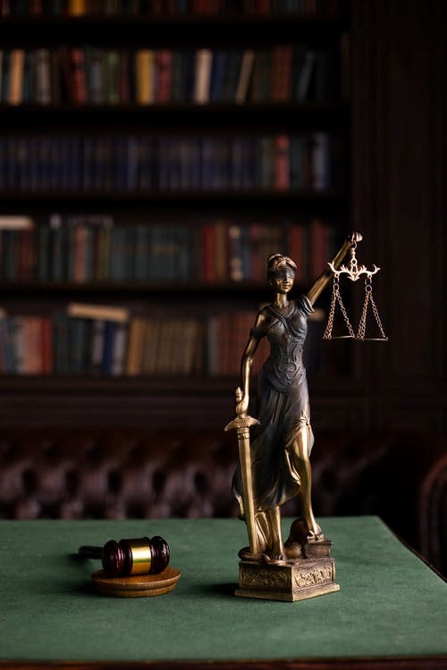 A table in a law office with a judge's hammer, a statue of a woman holding a balance scale, and a sword.